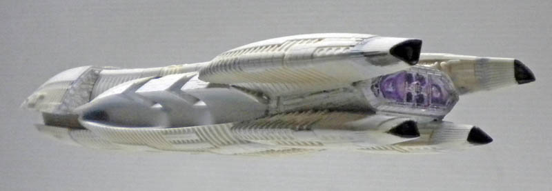 Maquette du vaisseau Battlestar Galactica vue de profil, coque blanche détaillée et cockpit éclairé violet