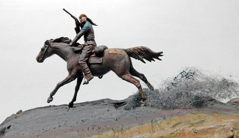 Figurine d'un guerrier indien au fusil galopant à cheval sur un diorama rocheux