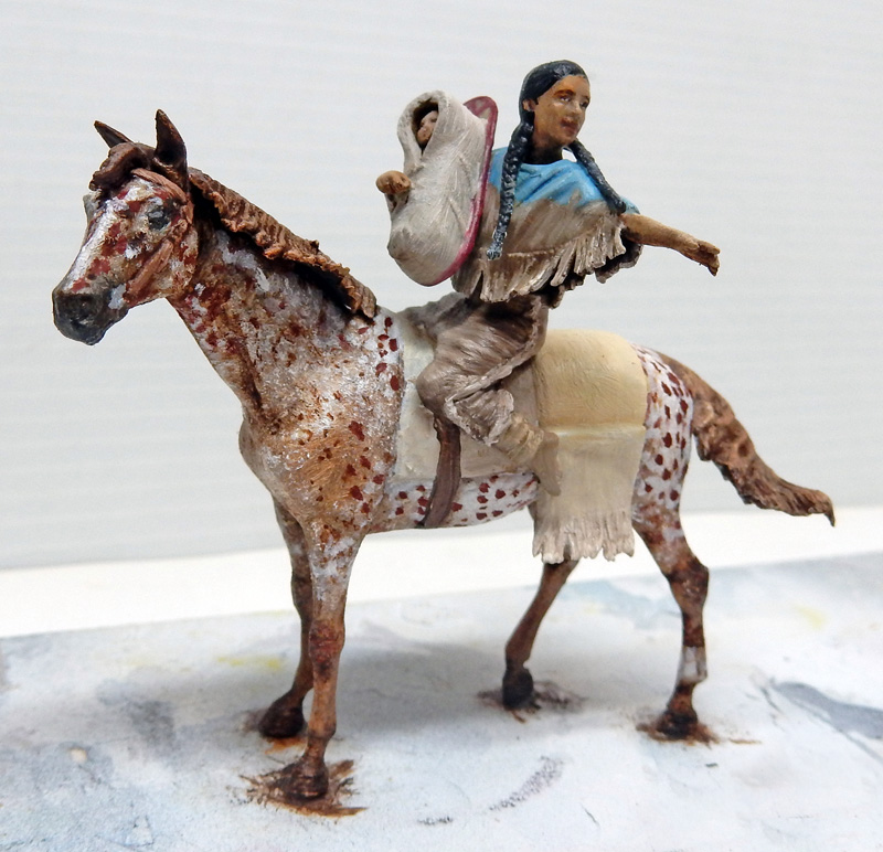 Figurine peinte d'une femme amérindienne portant son bébé à cheval sur un appaloosa tacheté
