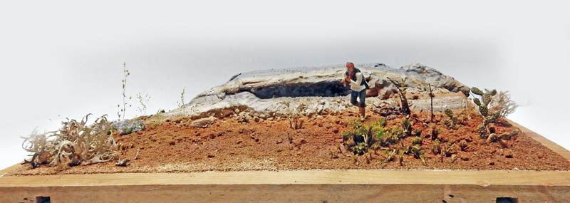 Diorama de maquette représentant un guerrier indien gravissant une colline rocheuse à la végétation désertique