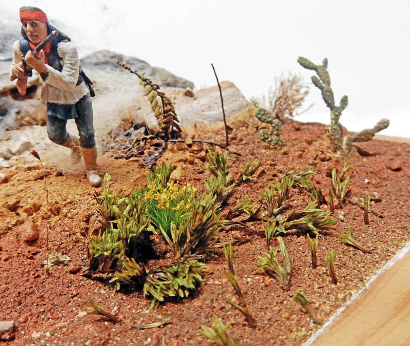 Figurine d'Indien armé d'un fusil progressant dans un diorama désertique avec cactus et végétation
