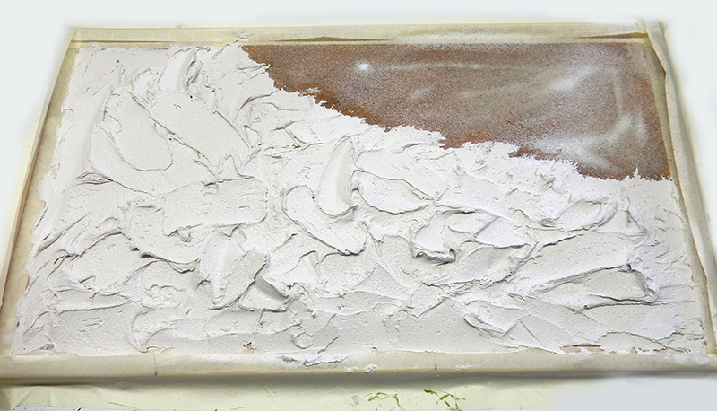 Application d'enduit blanc à la spatule sur un socle de diorama en préparation