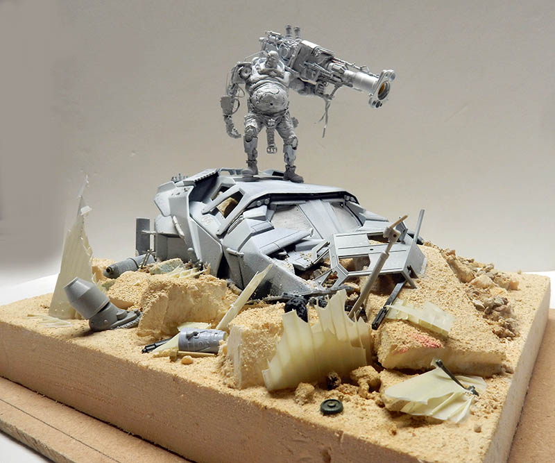 Maquette de cyborg armé dressé sur un véhicule détruit dans un diorama de débris