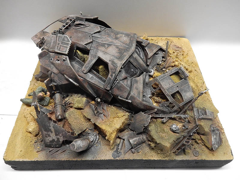 Diorama de maquette montrant un véhicule cyborg rouillé écrasé parmi des débris avec une figurine de soldat