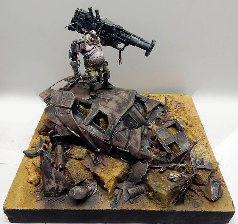 Diorama d'un cyborg massif armé d'un canon, debout sur l'épave d'un véhicule au milieu de débris