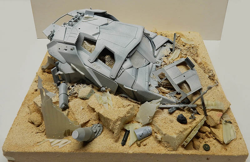 Maquette de véhicule cyborg gris écrasé dans un diorama de sable avec débris épars