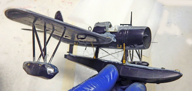 Maquette de l'hydravion Vought OS2U Kingfisher bleu foncé tenue par une main gantée