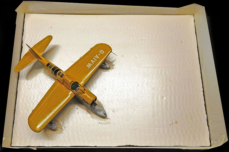 Maquette de Vought OS2U Kingfisher peinte en jaune doré, immatriculée G-AIVW, posée sur support blanc