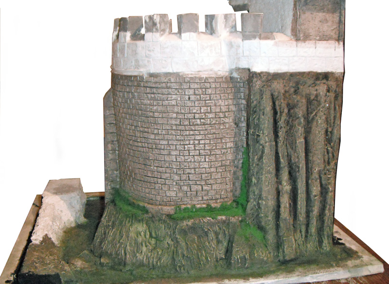 Maquette d'une tour de donjon crénelée en pierre dressée sur un éperon rocheux