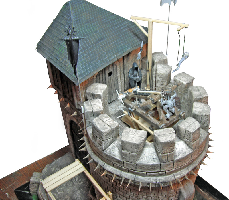Maquette de donjon médiéval avec créneaux en pierre, toit d'ardoise et figurines armées au sommet