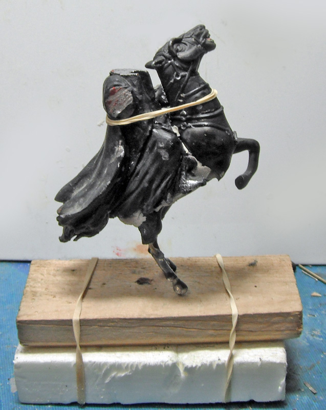 Figurine de cavalier sur cheval cabré en cours d'assemblage maintenue par élastiques sur support bois