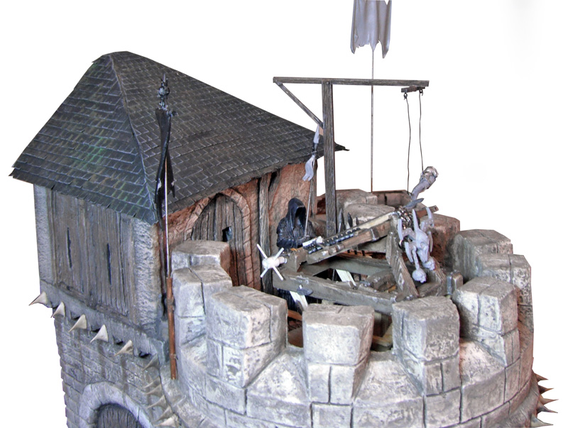 Sommet d'une maquette de donjon médiéval avec toit, potence et squelette suppliciés sur remparts crénelés