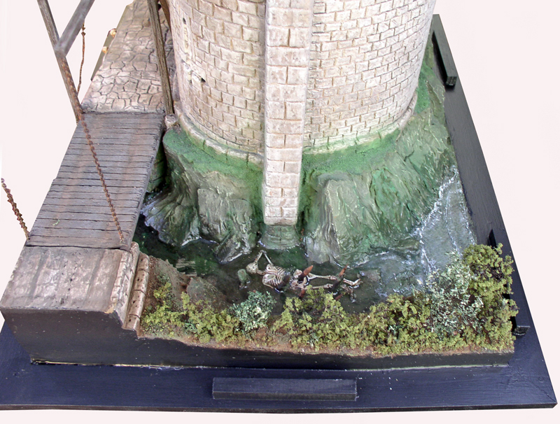 Base en pierre d'une maquette de donjon entourée d'eau avec pont-levis et squelette
