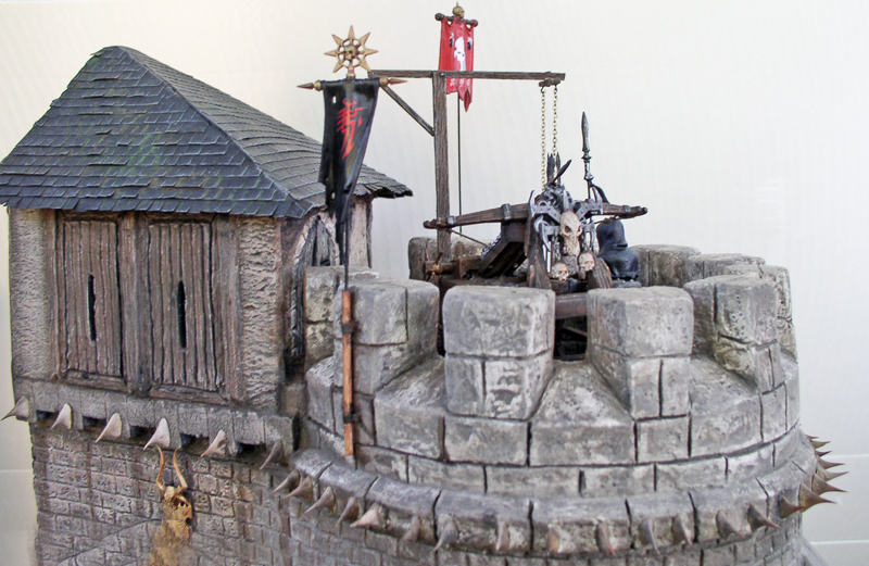 Sommet d'une tour de donjon en pierre avec bannières rouge et noire, balise et crânes