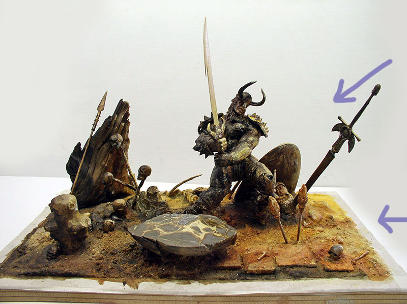 Diorama d'un guerrier cornu brandissant une épée parmi crânes et lances, flèches indiquant détails