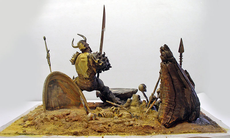 Diorama d'un guerrier casqué à cornes brandissant une épée parmi des ossements et armes
