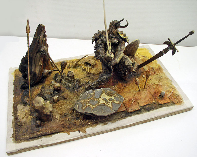 Diorama d'un guerrier cornu en armure sur un terrain désertique jonché de crânes et de lances