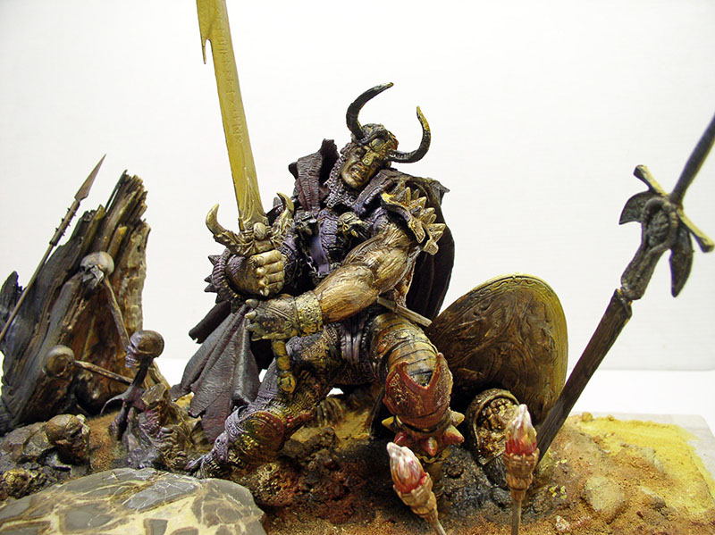 Figurine de guerrier cornu assis sur un diorama de champ de bataille avec épées et boucliers