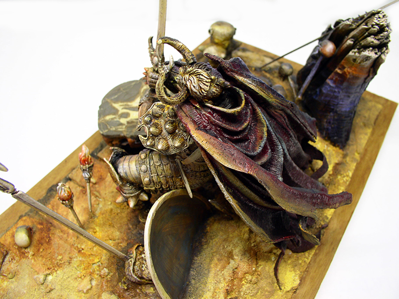 Figurine fantastique cornue drapée de cape pourpre sur diorama de sable doré