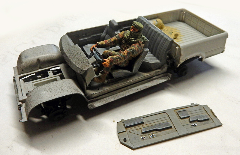 Figurine de chauffeur en treillis assise dans la cabine ouverte d'un camion maquette en montage