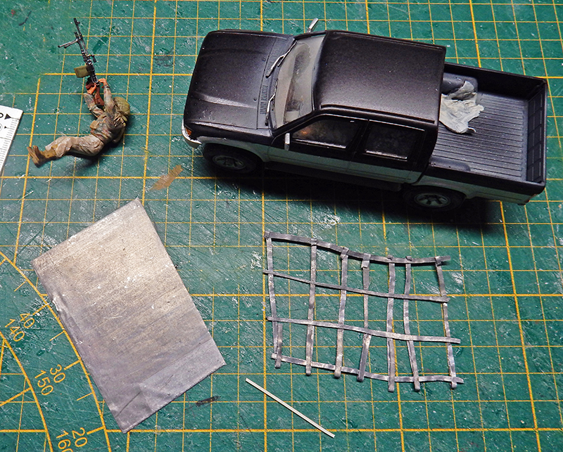 Maquette de pick-up noir, figurine de soldat et grillage sur tapis de découpe vert