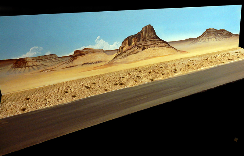 Diorama de paysage désertique avec route, montagnes rocheuses et fond peint de ciel bleu