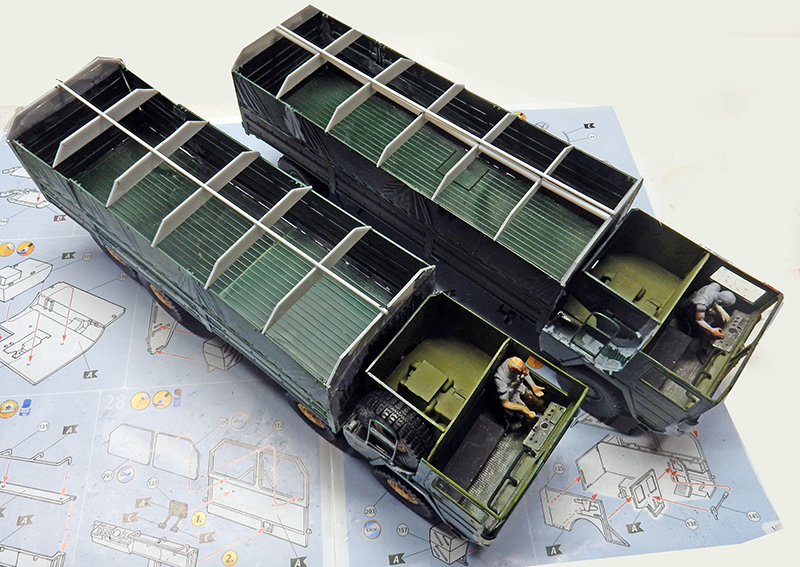 Deux maquettes de camions militaires avec figurines de conducteurs, posées sur une notice de montage