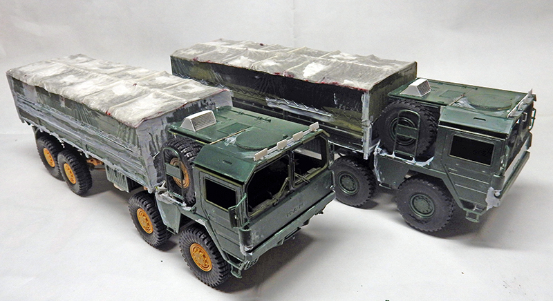 Deux maquettes de camions militaires verts bâchés vieillis, vus de trois quarts avant