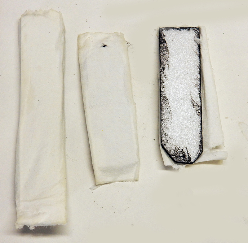 Trois bandes de tissu blanc roulées, la dernière marquée au crayon noir