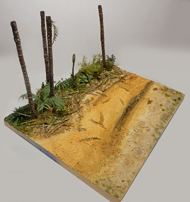 Décor de diorama en construction avec piste sablonneuse, palmiers et végétation tropicale sur socle