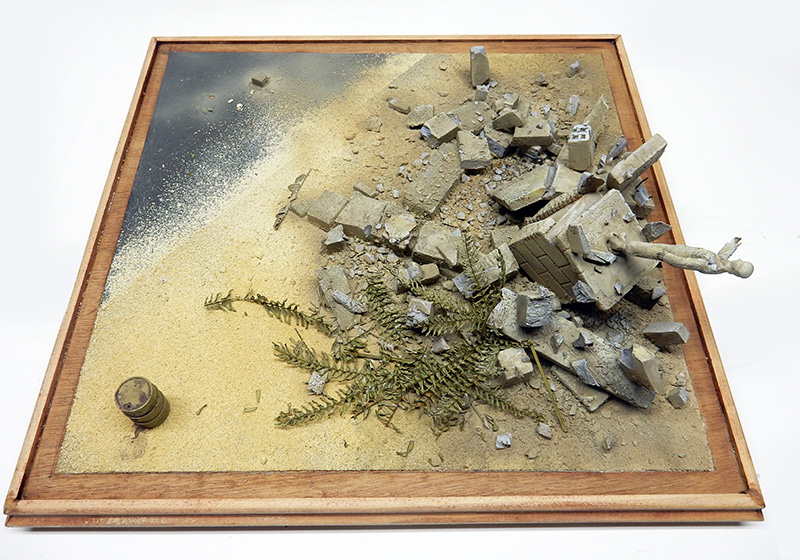 Socle de décor encadré de bois : sable, gravats, végétation sèche et bidon