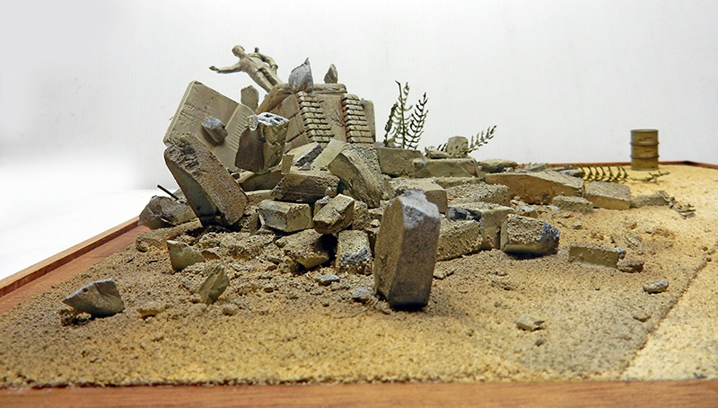 Base du diorama en cours : ruines de béton et statue effondrée sur sol sablonneux