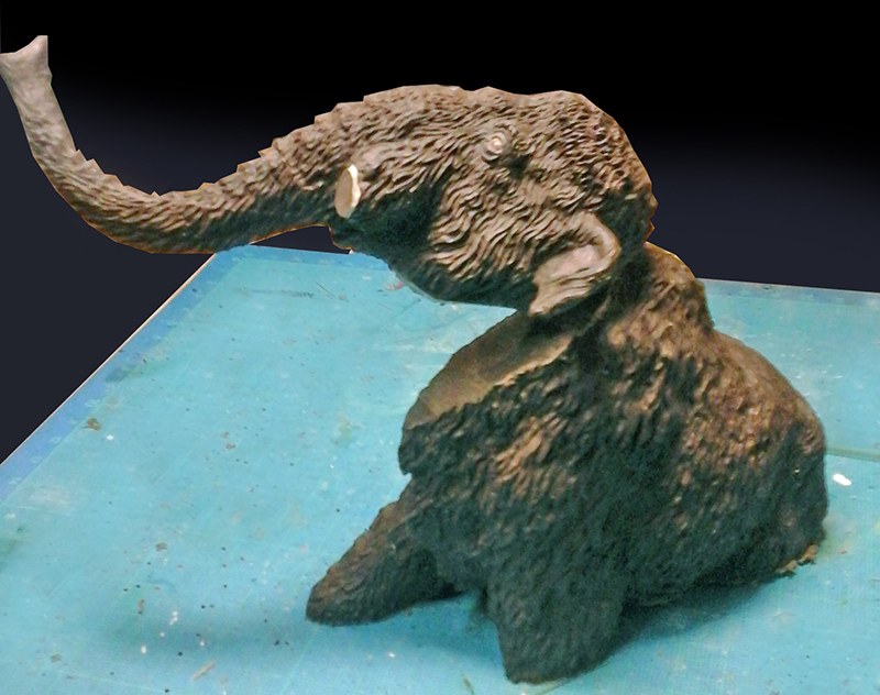 Buste de maquette de mammouth laine sculpté trompe levée posé sur tapis de découpe
