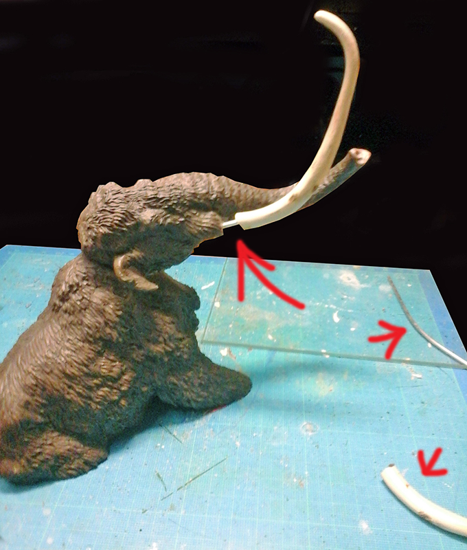 Maquette de mammouth avec défenses, flèches rouges indiquant les pièces sur tapis de découpe bleu