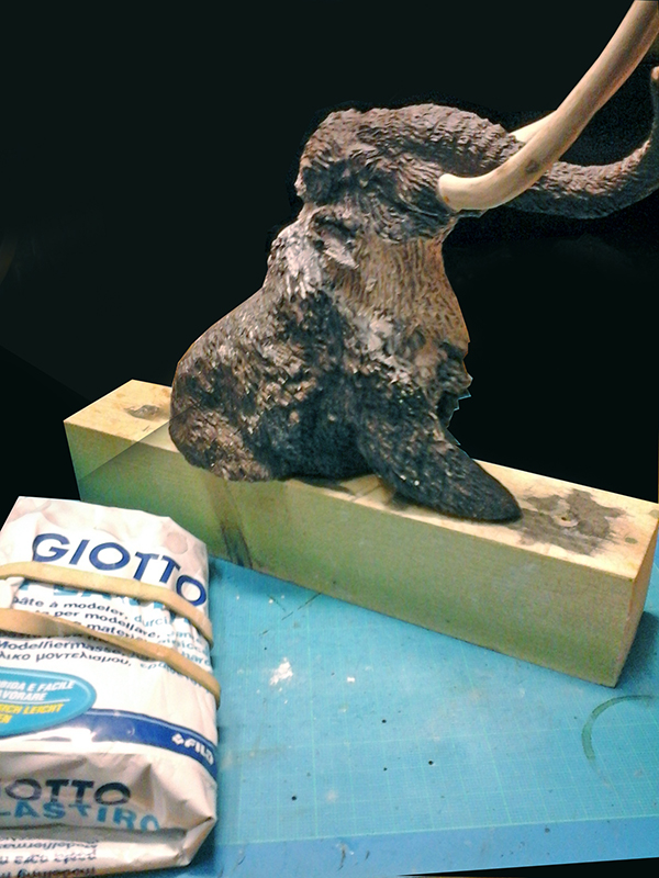 Maquette de mammouth sculptée en pâte à modeler sur socle bois près d'un sachet Giotto