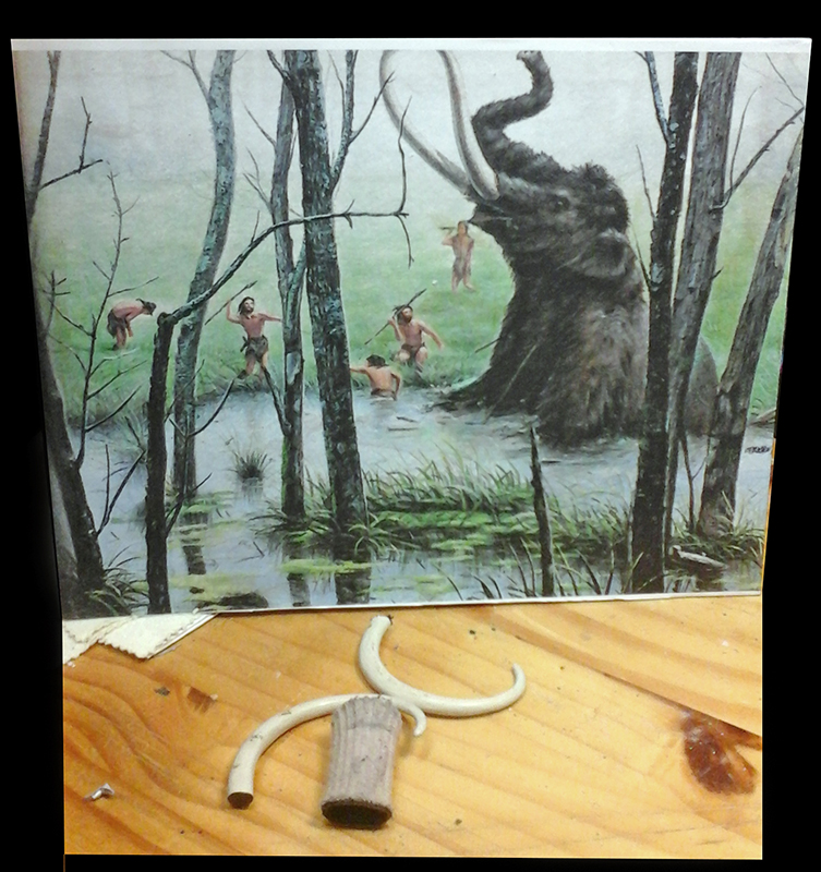 Défenses et trompe en cours de fabrication devant illustration de chasseurs préhistoriques attaquant un mammouth