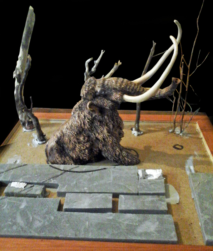 Maquette de mammouth laineux aux longues défenses sur un diorama avec arbres dénudés en construction
