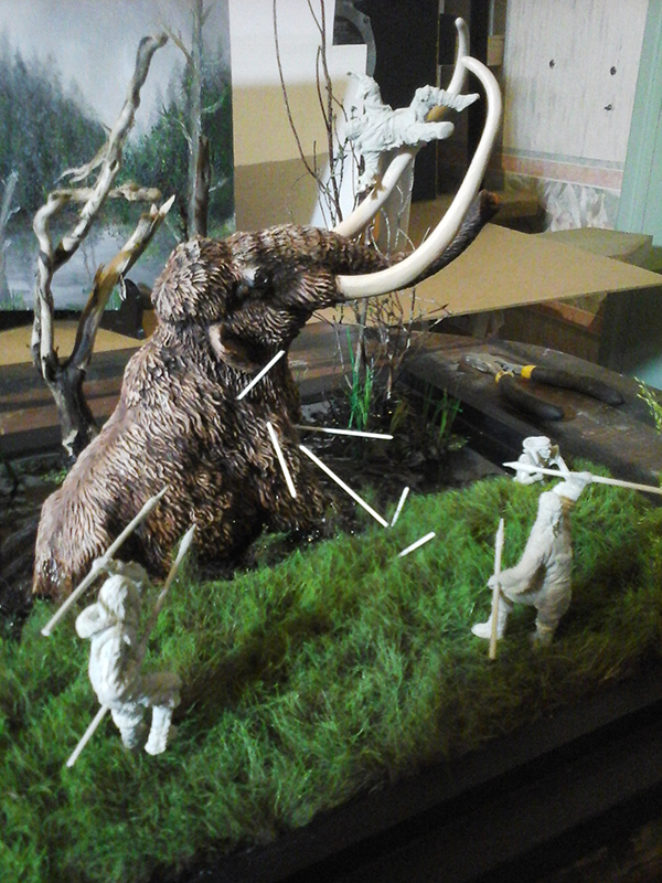 Diorama d'un mammouth attaqué par des chasseurs préhistoriques lançant des sagaies dans un marais