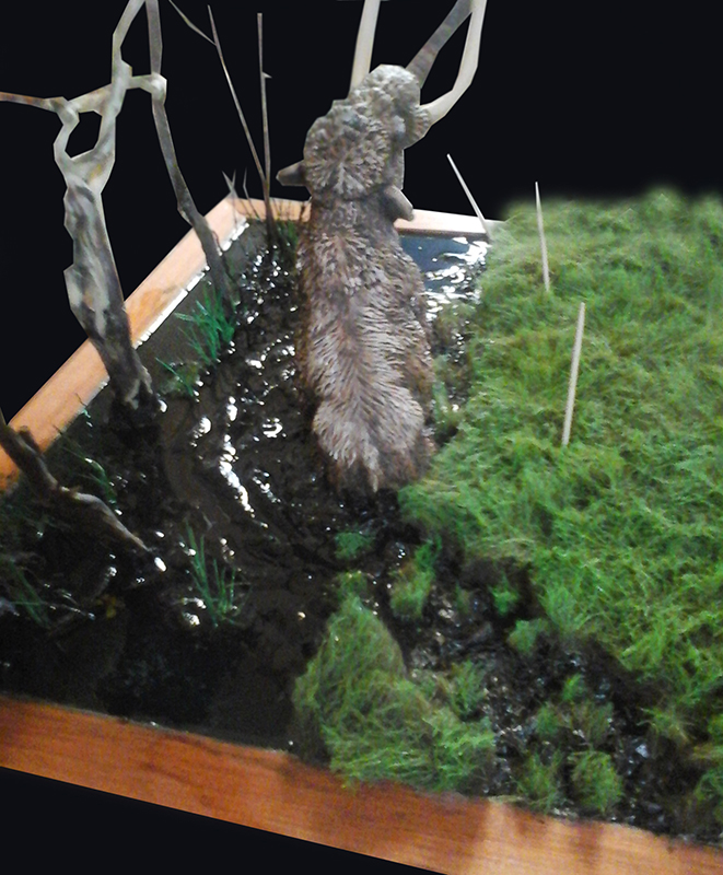 Maquette de mammouth laineux progressant dans un marécage boueux d'un diorama avec herbes et arbres
