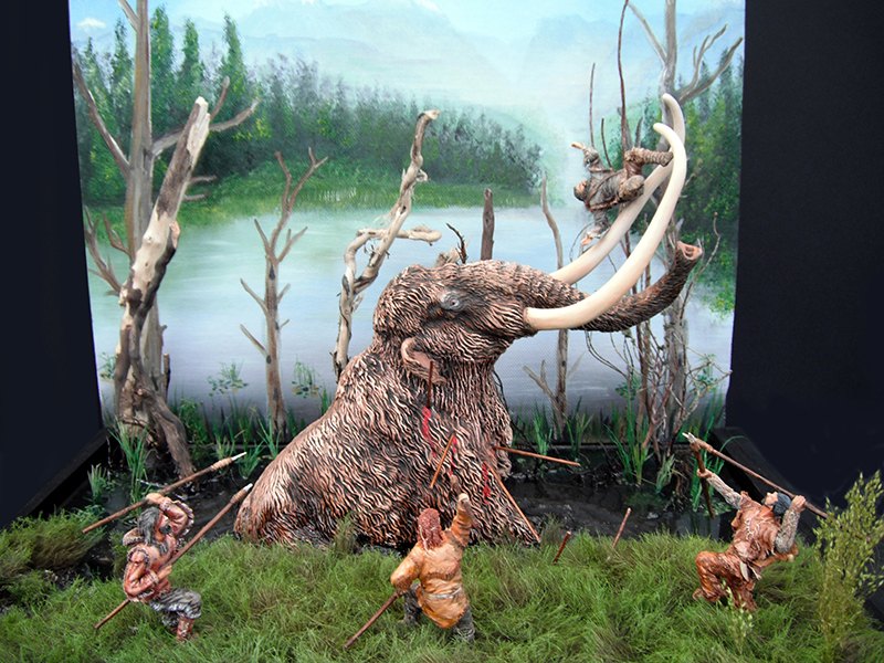 Diorama de maquette montrant un mammouth aux longues défenses attaqué par des chasseurs préhistoriques armés de lances