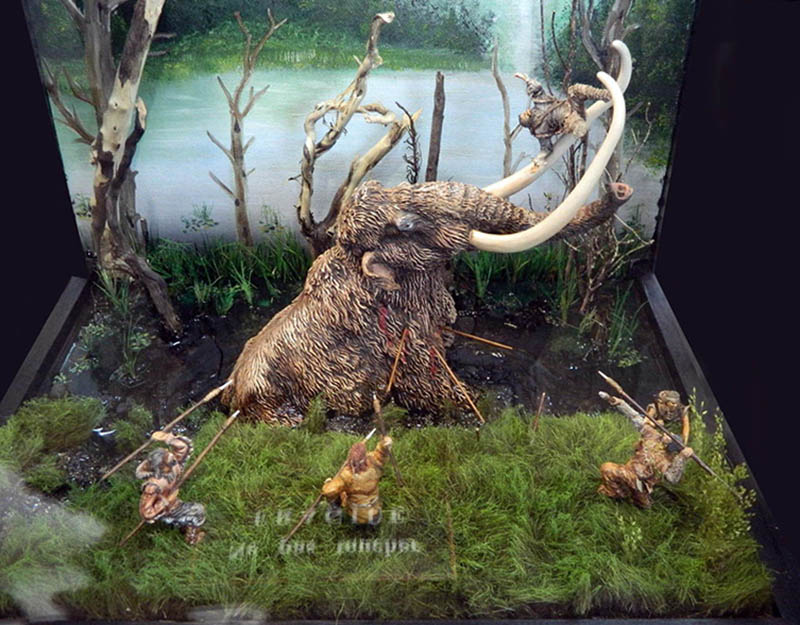 Diorama de chasse au mammouth enlisé attaqué par des chasseurs préhistoriques avec lances près d'un marais