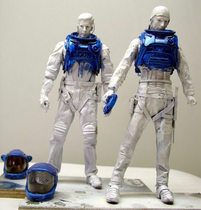 Deux figurines d'astronautes en cours de peinture avec armures bleues et casques posés devant