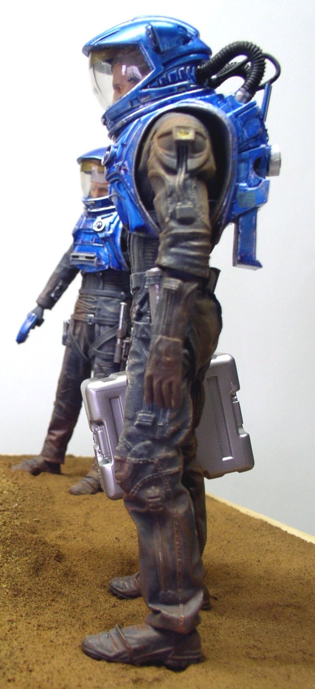 Deux figurines d'astronautes en combinaison bleue portant casque et mallette sur sol martien ocre