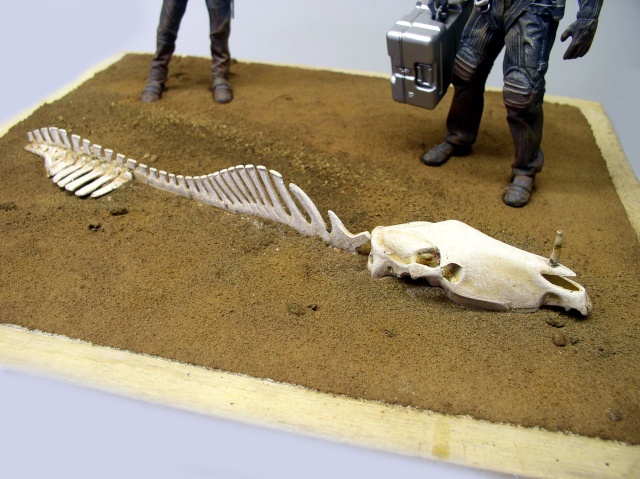 Diorama de sable avec squelette d'animal et figurines de personnages portant une mallette métallique