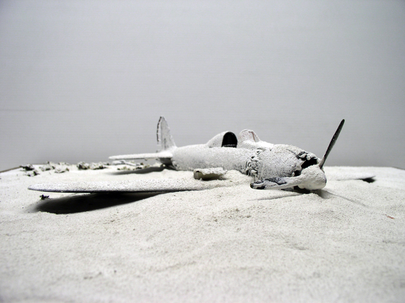 Maquette de Mitsubishi A6M5 sans peinture posée sur un diorama de sable clair