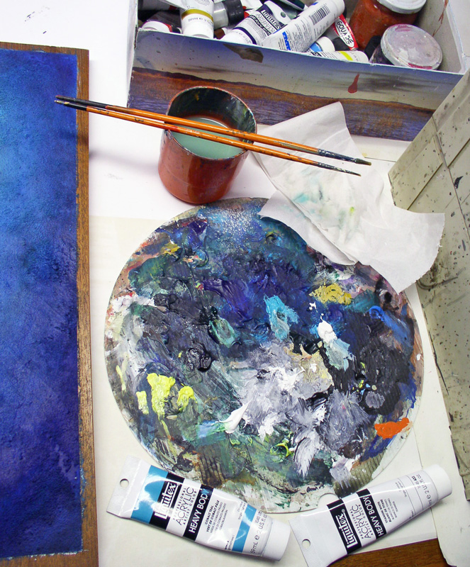 Palette ronde couverte de peinture acrylique, pinceaux fins, pot et tubes sur le plan de travail