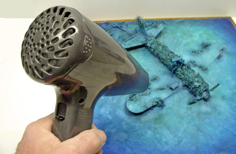 Sèche-cheveux dirigé vers le diorama sous-marin représentant l'épave du Mitsubishi A6M5 immergée