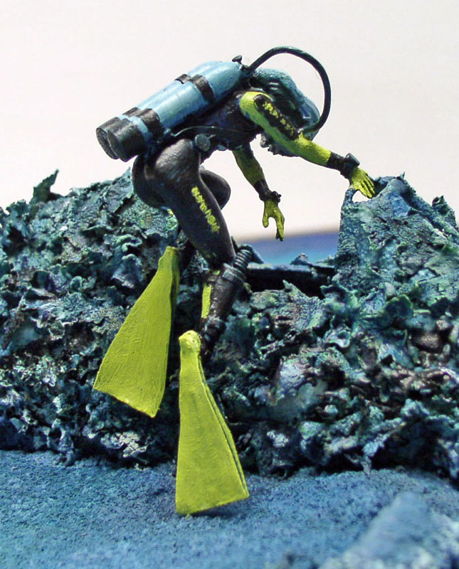 Figurine peinte de plongeur sous-marin avec palmes jaunes sur diorama de rochers immergés