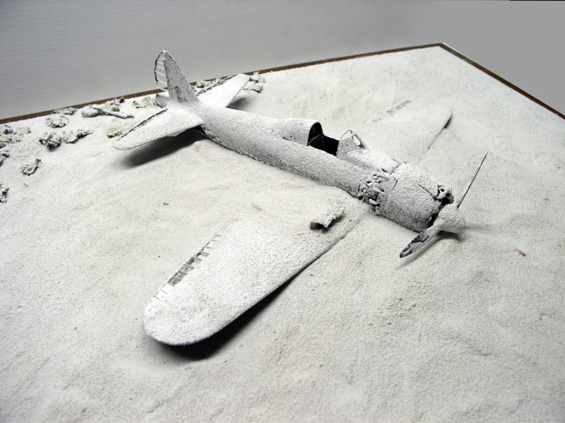 Maquette du Mitsubishi A6M5 recouverte d'un apprêt blanc posée sur un diorama de sable