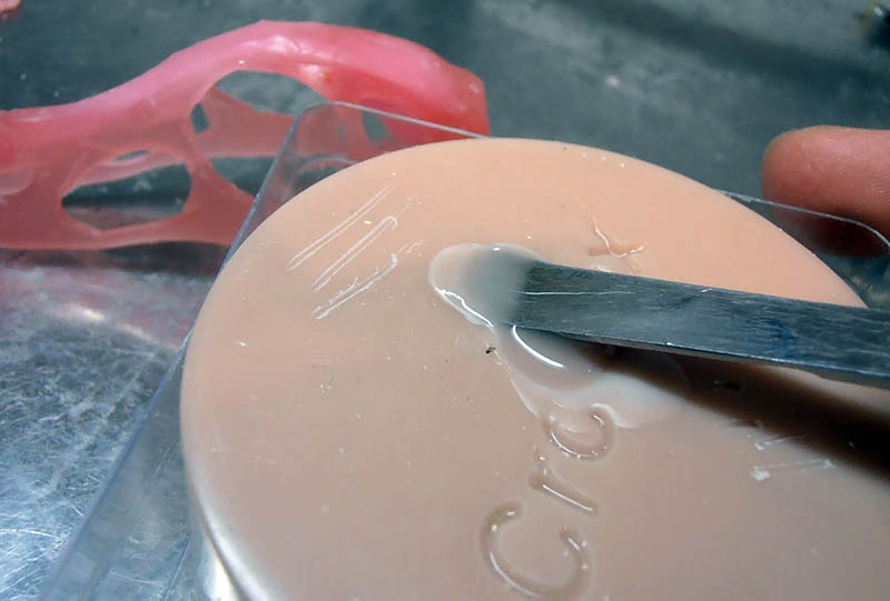 Spatule métallique étalant une résine claire sur un couvercle, moulage rose en arrière-plan